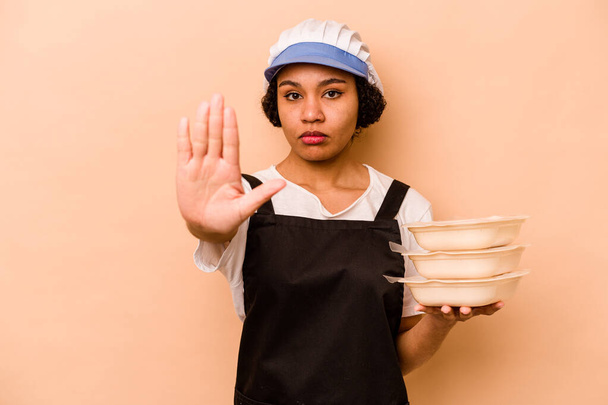 Mladý kuchař dobrovolník Afroameričanka izolované na béžové pozadí stojící s nataženou rukou ukazující stopku, brání vám. - Fotografie, Obrázek