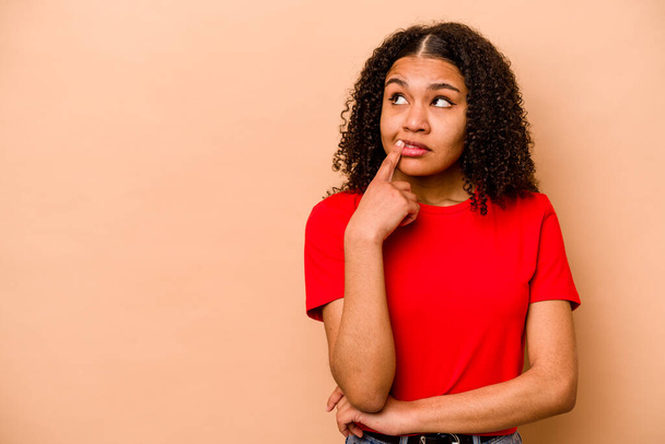 Giovane donna afroamericana isolata su sfondo beige guardando lateralmente con espressione dubbia e scettica. - Foto, immagini