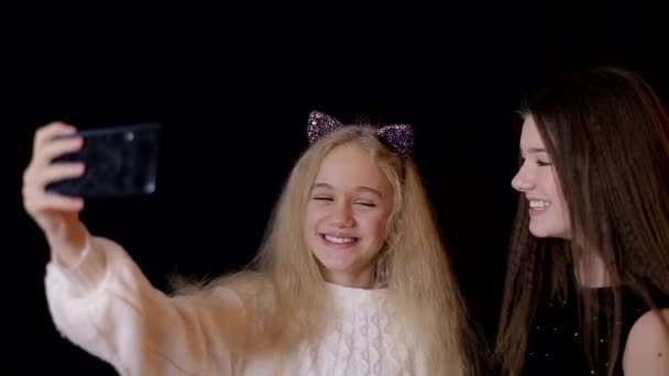Two sisters make selfie on the phone and smile, a black background - Materiał filmowy, wideo