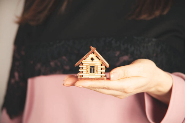женщина рука держа деревянный дом модель на сером фоне - Фото, изображение