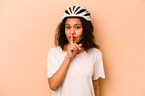 Giovane donna ispanica che indossa un casco bici isolato su sfondo blu mantenendo un segreto o chiedendo silenzio. - Foto, immagini