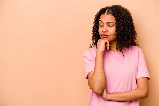 Young African American woman isolated on beige background looking sideways with doubtful and skeptical expression. - Photo, Image