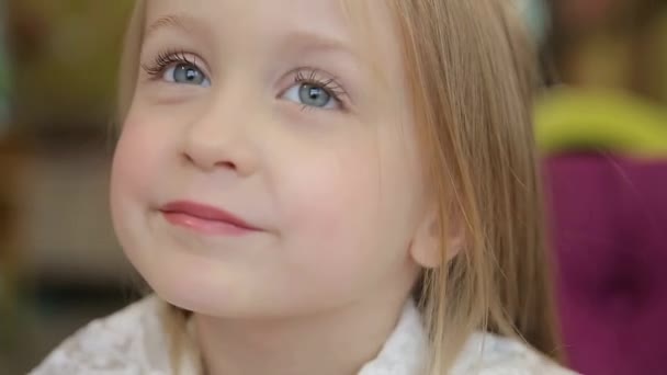 Ein schönes kleines Mädchen mit hellen Haaren, das mit einem sanften Lächeln in die Kamera schaut und das Fotoshooting in der Schule behandelt. - Filmmaterial, Video