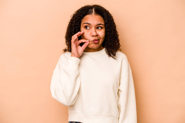 Young African American woman isolated on beige background with fingers on lips keeping a secret. - Photo, Image