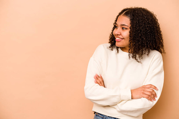 Young African American woman isolated on beige background smiling confident with crossed arms. - Photo, Image
