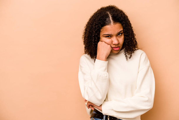 Young African American woman isolated on beige background who feels sad and pensive, looking at copy space. - Photo, image
