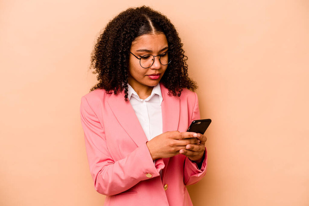 Junge afroamerikanische Geschäftsfrau hält Handy isoliert auf beigem Hintergrund - Foto, Bild