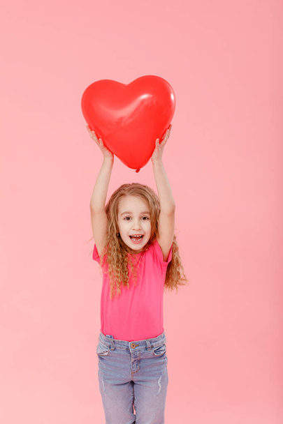 Suloinen pieni tyttö, jolla on punainen ilmapallo sydämen muotoinen vaaleanpunainen tausta. Äitienpäivä, Ystävänpäivä, rakkaus, tunne, perheen käsite - Valokuva, kuva