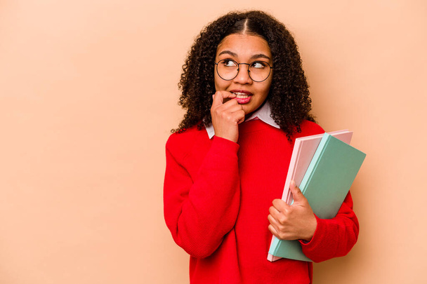 Jonge student Afro-Amerikaanse vrouw geïsoleerd op beige achtergrond ontspannen denken over iets op zoek naar een kopieerruimte. - Foto, afbeelding