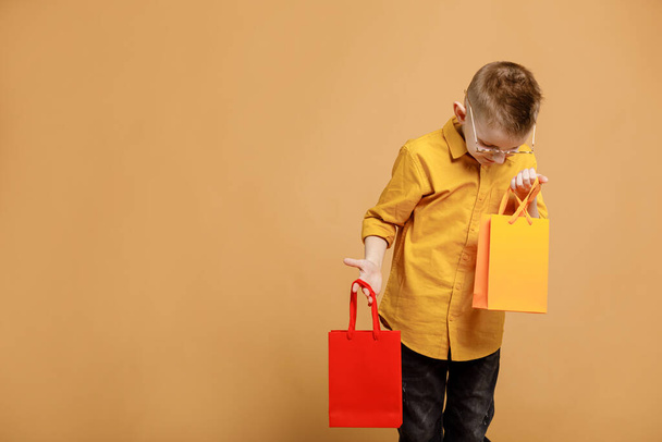 Shopping on black friday. Little boy holding shopping bags on yellow background. Shopper with many colored paper bags. Holidays sales and discounts. Cyber monday. High quality photo. - Fotografie, Obrázek