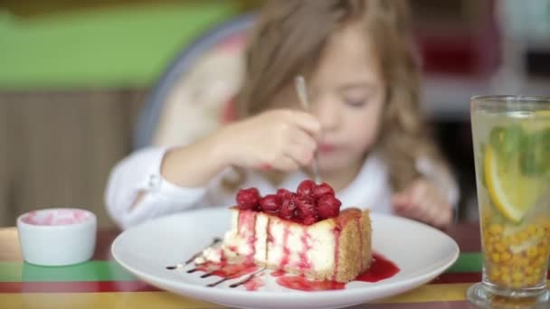 aranyos kislány tortát eszik. Csinos kislány tortával és eperrel. A gyerek desszertet eszik. lány eszik kanállal az asztalnál - Felvétel, videó