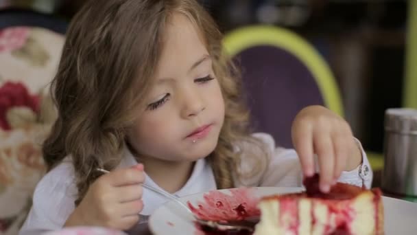 cute little girl eating cake. pretty little girl with cake and strawberries. child eating dessert. girl eating with spoon by the table - Кадры, видео