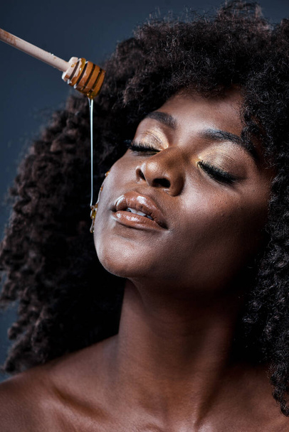 Honey is perfect for both preventing and treating acne. Shot of a beautiful young woman holding a honey dipper against her face. - Foto, immagini