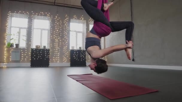Aerial yoga - a young woman spins in a hammock suspended from the ceiling - Filmati, video