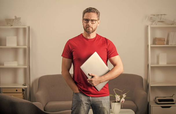 poważny facet w czerwonej koszuli i okulary trzymać pc, freelancer - Zdjęcie, obraz