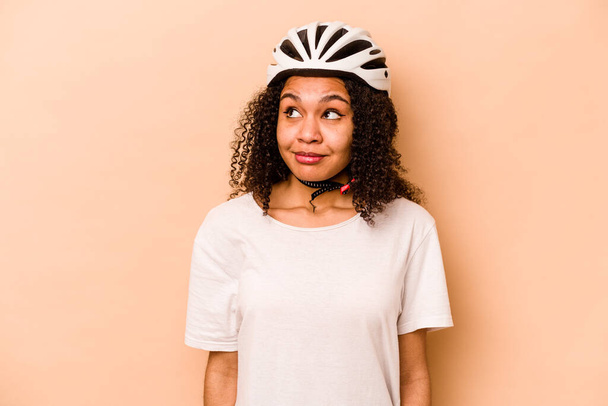 Молодая испаноязычная женщина в шлеме велосипеде на синем фоне мечтает о достижении целей и целей - Фото, изображение