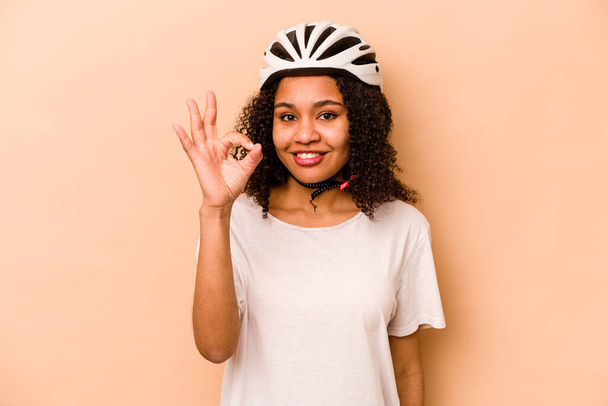若いですヒスパニック女性身に着けていますヘルメット自転車隔離上の青背景陽気で自信を持ってショーokジェスチャー. - 写真・画像