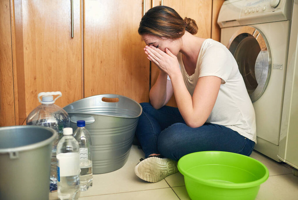 Feeling stressed about the water crisis. Shot of a beautiful young woman crying on the floor in the kitchen at home. - 写真・画像