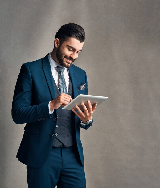 Tapped into the latest corporate trends. Studio shot of a stylishly dressed young businessman using a digital tablet against a grey background. - Foto, Bild
