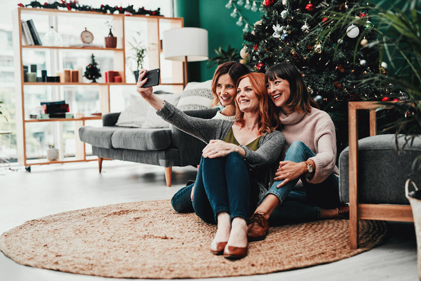 Czas na wspólne selfie. Zdjęcia trzech atrakcyjnych kobiet w średnim wieku robiących autoportrety razem z telefonem komórkowym w domu w czasie świąt Bożego Narodzenia. - Zdjęcie, obraz