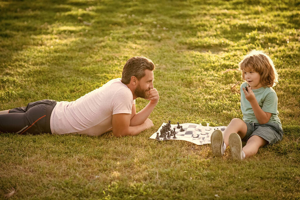 father and son playing chess on grass in park. fathers day. happy family. parenthood and childhood. - Foto, Imagen