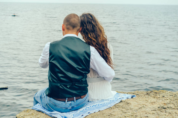 man and woman sitting on a stone and looking at the sea - Foto, Imagen