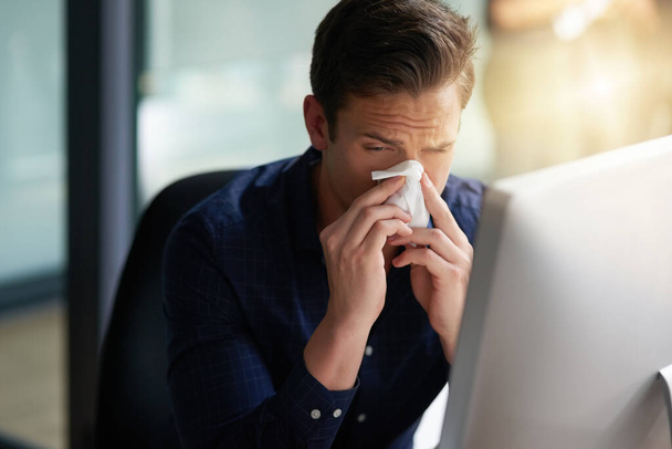 This cold is starting to torture me. Shot of a young businessman blowing his nose in an office. - Photo, Image