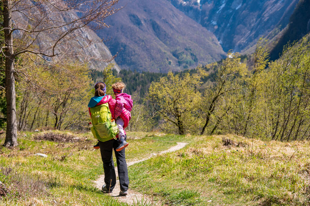Anne orman çayırında yürürken kızını kucaklıyor. Aktif aile hayatı açık havada. - Fotoğraf, Görsel