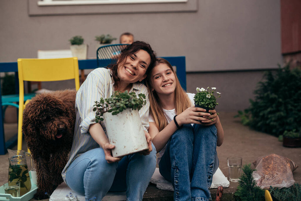 happy mother and daughter holding plants and looking at camera - Zdjęcie, obraz