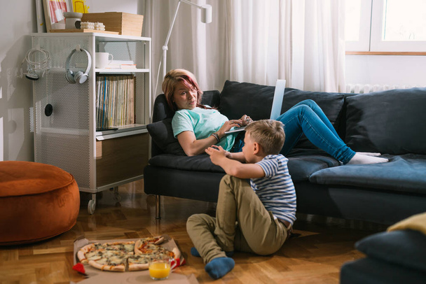 young caucasian boy relaxing at home with his mom. they having pizza snack and talking - Fotografie, Obrázek