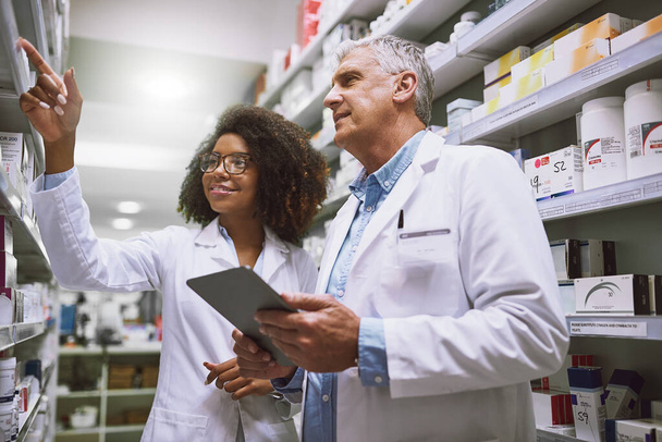 We need more of this meds. Shot of two focused pharmacist walking around and doing stock inside of a pharmacy. - Photo, Image