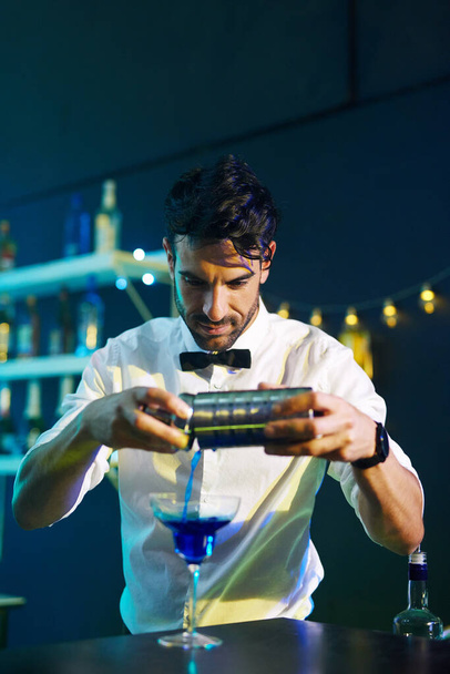 Agitado, agitado, servido. Foto de un apuesto joven barman sirviendo un cóctel en una copa en un club nocturno. - Foto, Imagen