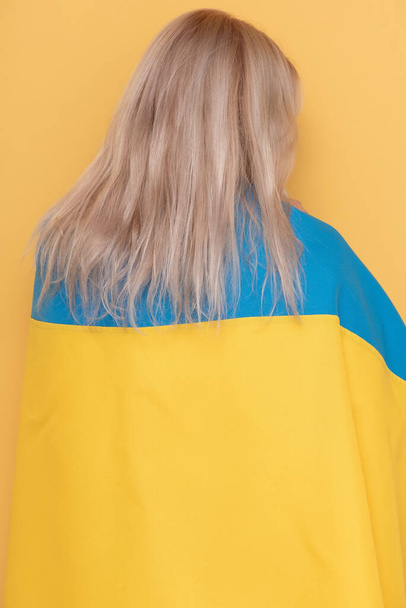 Mujer de vuelta a la cámara sobre un fondo amarillo. Mujer con paño azul-amarillo en los hombros. - Foto, Imagen