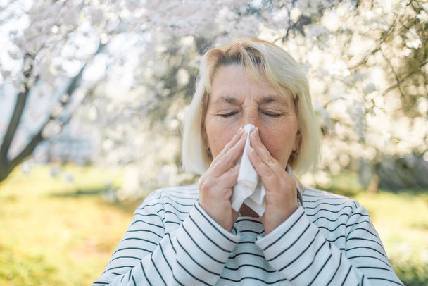 50s woman sneezing in park. Allergy, flu, virus concept. - Photo, Image