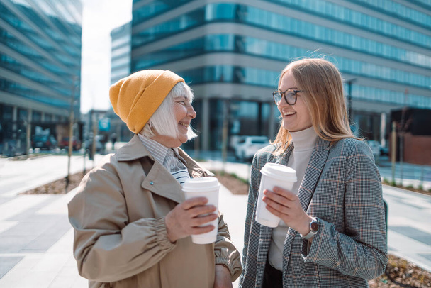 Portrait of two middle age women talking at office park while on coffee break. Businesswomen relaxing while drinking coffee and chatting with each other.  - Фото, изображение
