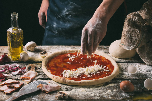 The chef sprinkles mozzarella cheese on a pizza base  - Foto, Bild