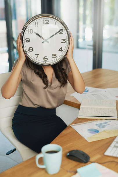 Shes got time on her mnind. Shot of an unidentifiable businesswoman holding a clock in front of her face while sitting at her desk. - Photo, image
