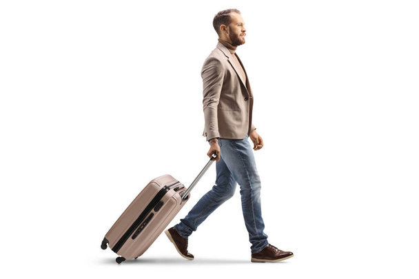 Full length profile shot of a man walking and pulling a suitcase isolated on white background - Fotografie, Obrázek
