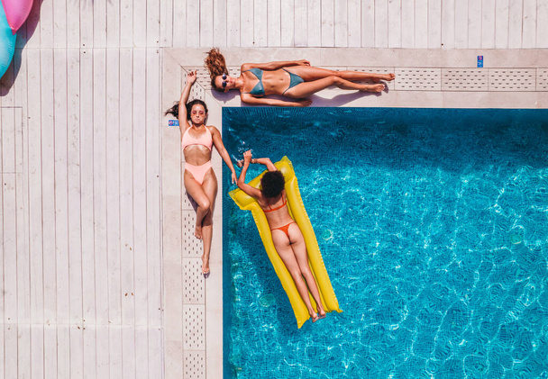 Друзья в купальниках, которые загорают на шезлонге в бассейне - Фото, изображение