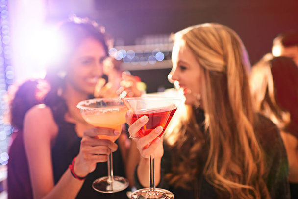 Clink before you drink. Shot of two young women drinking cocktails at a party. - Foto, imagen