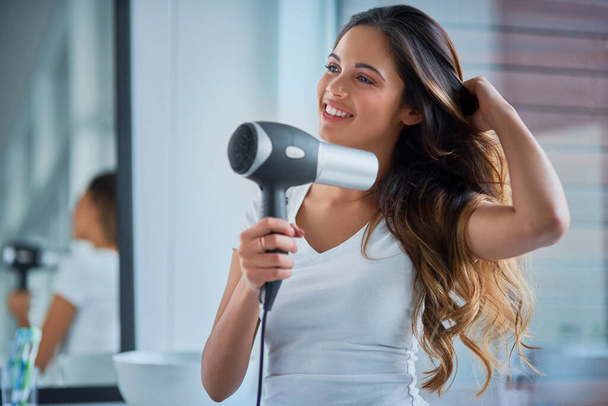 Putting great care into her hair. Shot of an attractive young woman blowdrying her hair in the bathroom. - Foto, Imagem