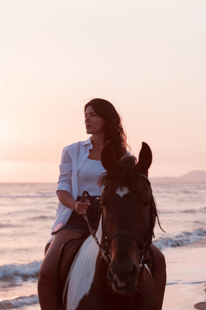 Woman in summer clothes enjoys riding a horse on a beautiful sandy beach at sunset. Selective focus  - Photo, image
