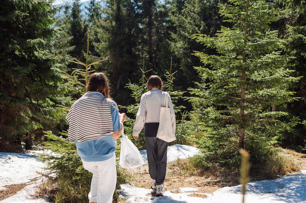 Kaksi naista mädäntyneissä peuran vaatteissa kävelee lumisella polulla vuorilla, aktiivinen virkistys vuoristoalueella keväällä. - Valokuva, kuva