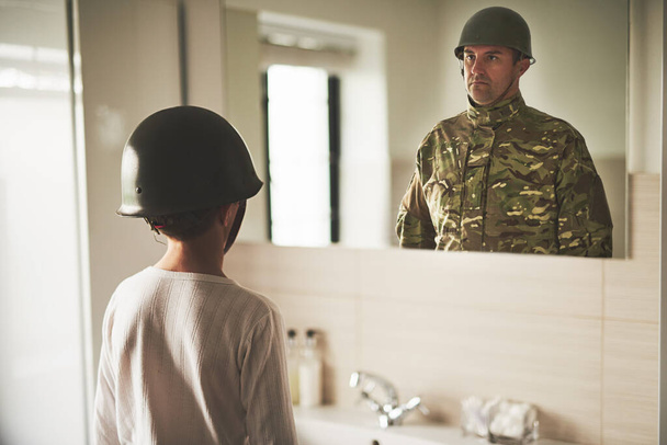 Tatusiu, wracaj do domu. Zdjęcie z tyłu młodego chłopca w wojskowym hełmie, oglądającego odbicie ojca w lustrze.. - Zdjęcie, obraz