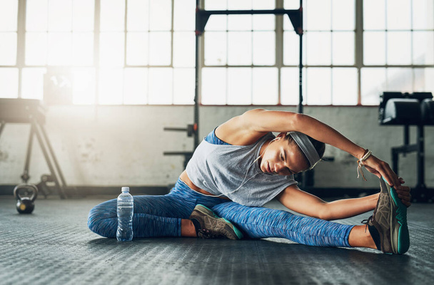 Strength is her middle name. Shot of a young attractive woman stretching in a gym. - Foto, immagini