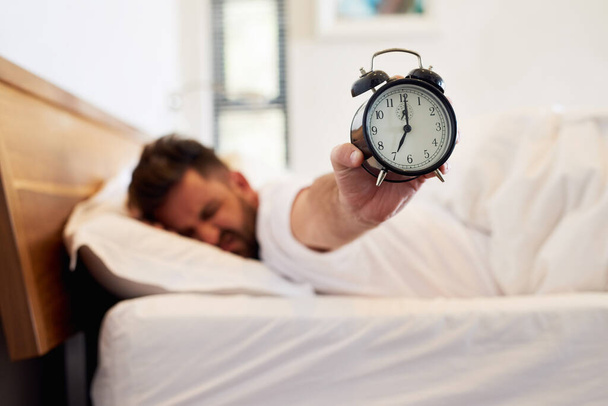 Время встретиться лицом к лицу. Обрезанный снимок молодого человека, держащего будильник, когда он просыпается из постели дома. - Фото, изображение