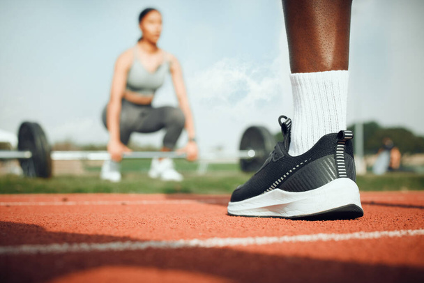 Toegewijd aan fitness. Close-up shot van een onherkenbare mannelijke atleet buiten staan, terwijl een vrouw oefent met gewichten op de achtergrond. - Foto, afbeelding