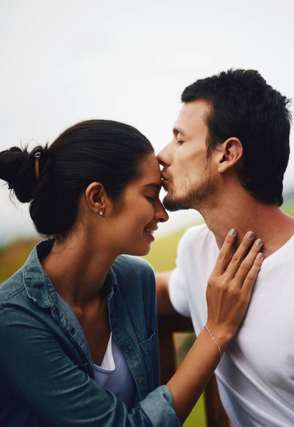 額のキスは、世界で最も美しい感じ。公園でロマンチックな一日を過ごす愛情のある若いカップルのショット. - 写真・画像