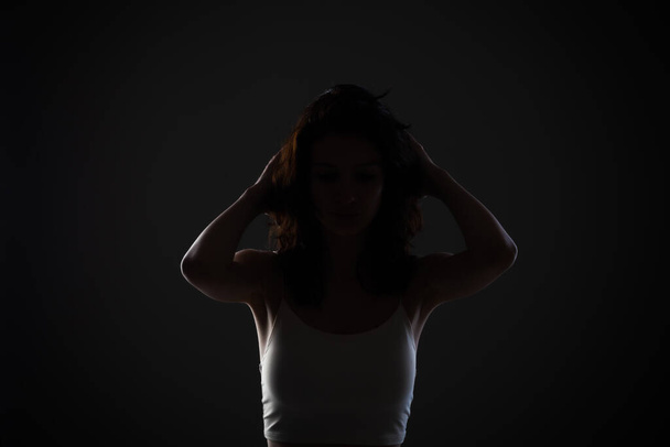 Side lit half silhouette portrait of a beautiful teenage girl in studio against dark background. - Фото, изображение