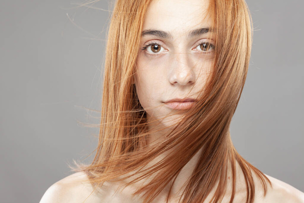 Beautiful dark burnt orange windy hair girl. Studio portrait with serious face expression against gray background. - Fotografie, Obrázek